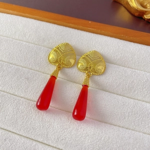 Close-up of vintage heart stud earrings with red teardrop pendants on white velvet