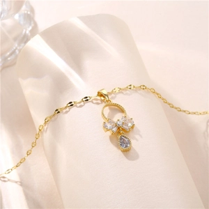 Elegant gold bow necklace with clear zircon teardrop pendant on a beige display stand