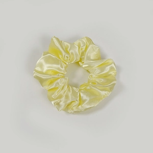 Detail view of a pale yellow satin scrunchie with smooth silk texture and ruched design