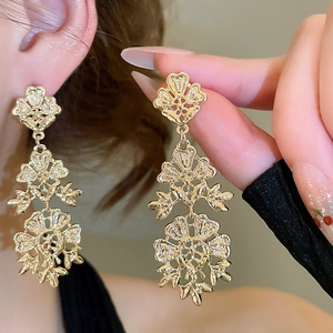 Detail of model wearing golden hollow flower fringe earrings with three-layer design