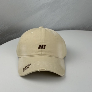 Close-up of distressed khaki baseball cap with brown letter embroidery and frayed brim detail