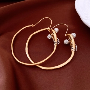 Detail of gold irregular hoop earrings with crystal-encrusted sphere on brown fabric
