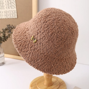 Detail of dark brown plush bucket hat with a decorative gold bow buckle on wood stand
