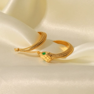 Gold-toned stainless steel snake hoop earrings with green crystal eyes on silk fabric