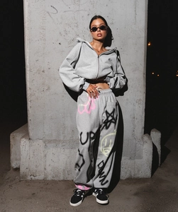 Tenue streetwear avec sweat à capuche gris et pantalon à graffiti devant un mur