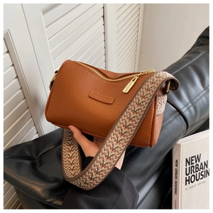 Detail der dunkelbraunen Kissen-Tasche aus Leder mit breitem Webgurt und Gold-Reißverschluss