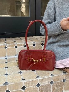Detail of vintage burgundy leather handbag with gold metal buckle on a shoulder strap