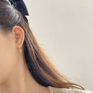 Detail of a minimalist gold S925 sterling silver cross earring worn by a model