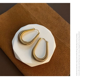 Detailed macro shot of gold U-shaped hoop earrings with textured ribbed surface on a tray