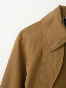 Detailed close-up of khaki trench coat collar and shoulder seams in twill fabric
