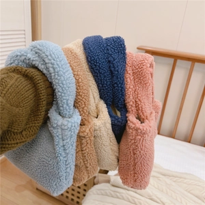 Détail de mini sacs à main en laine d'agneau pelucheuse en bleu, beige et rose sur lit doux