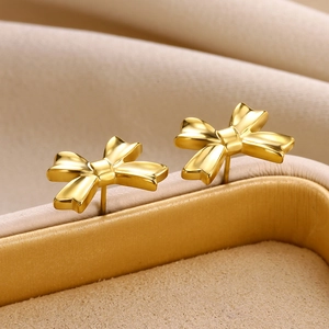 Macro shot of 3D golden bow stud earrings on a beige jewelry box with sharp metallic luster