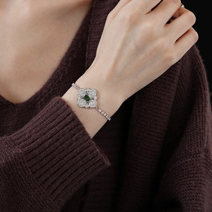 Close-up of a silver flower bracelet with a green gemstone on a model's wrist