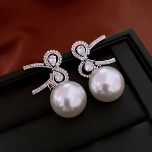 Detail of bow-shaped zircon earrings with round pearl drops on a black leather display