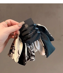 Detail of a large silk bow hair claw clip with floral print held in hand