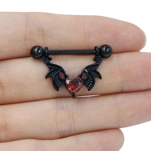Détail d'un piercing téton ailes de chauve-souris noires avec zircon cœur rouge