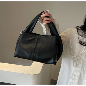 Detail of black pebbled leather handbag featuring elegant gold hardware and sturdy handle