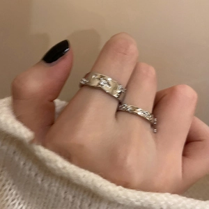Detail of silver S925 textured rings with cubic zirconia worn on a white sweater background