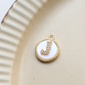 Macro shot of gold-plated letter J pendant with shell inlay and zircon details