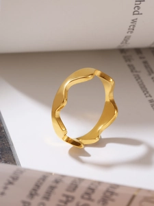 Detailed view of a wavy gold ring reflecting on minimalist book pages with soft shadows