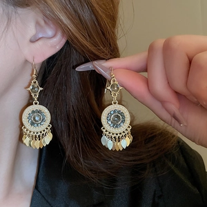 Close-up of bohemian gold tassel earrings with dark gemstones and pearl accents
