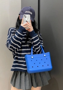 Detail of bright blue EVA tote bag with hole pattern carried by a model in a mirror selfie