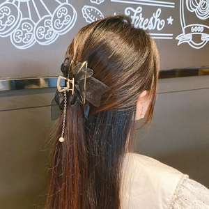 Detail of mesh bow hair claw with pearl tassel pendant worn in a half-up hairstyle