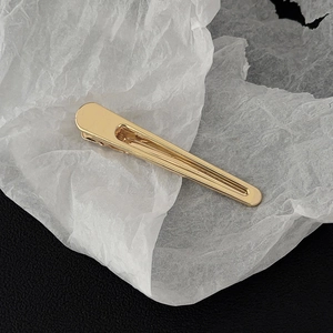 Detailed top view of a gold-plated alloy duckbill hair clip on a textured background