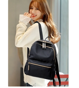 Detail showing back of black nylon backpack with golden zippers on female model