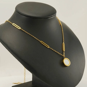 Detail of gold-plated necklace with white circular pendant on black mannequin display