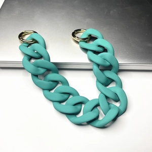 Close-up of matte teal acrylic bag chain with shiny gold metal ring clasps on flat surface