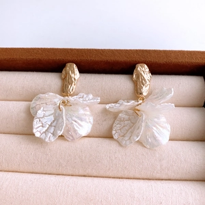 Detailed shot of pearlescent flower petal earrings with textured golden metal studs