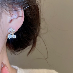 Detailed close-up of cherry stud earring with white zircon and gold plating on ear