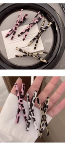 Detailed view of three leopard print bow hair clips in pink and gold on a black tray