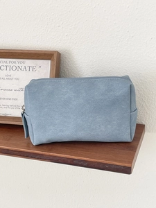 Detail view of a blue minimalist PU leather toiletry bag on a wooden shelf with frame