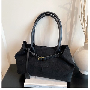 Detailed close-up of a black matte suede tote bag with golden buckle and sleek leather tag