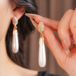 Detail of pavé crystal gold earrings featuring large white teardrop pearl pendants