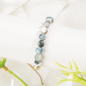 Detail of natural moss agate bead bracelet with a faceted gold bead on a white display