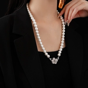 Detail of a pearl necklace with a zircon flower clasp worn on a black blazer