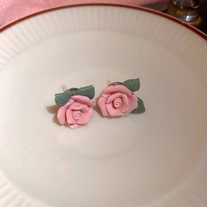 Macro di orecchini a lobo con rose rosa 3D e foglie verdi su un piatto di ceramica