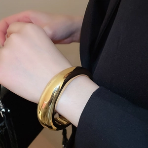 Vue détaillée d'un bracelet manchette doré poli avec rayures porté sur une manche noire