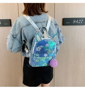 Detail of blue sequin unicorn backpack with silver horn and purple pompom charm on model