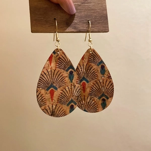 Detail of vintage teardrop leather earrings featuring ethnic leaf print on a wooden hanger