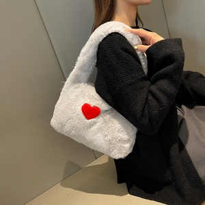 Close-up of white plush crossbody bag with red heart pattern worn on shoulder