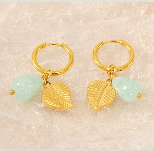 Détail de boucles d'oreilles feuille dorée avec perles vert clair sur fond de dentelle