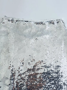 Dettaglio del tessuto con paillettes argento e paillettes tonde su gonna a spacco