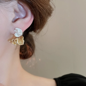 Detail of silver shell-shaped stud with pearl and gold pleated petal drop on model