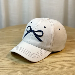 Detail of white denim baseball cap with navy blue bow embroidery on a textured fabric