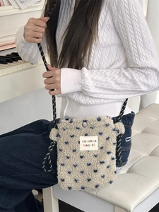 Mini plush lamb wool crossbody bag with navy heart patterns and rope strap on white piano