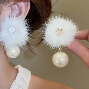 Close-up of white plush pom-pom earrings with crystal rhinestones and faux pearls